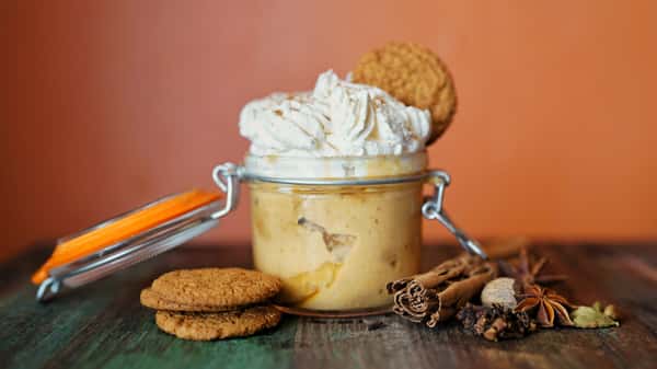 Jar dessert is artfully decorated with spices and cookies. A creamy topping completes the dessert, perfect for showcasing in a gallery.