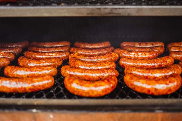Several rows of sausages sit on a grill rack. The sausage texture is semi-smooth and orange, and they look delicious and ready to eat.