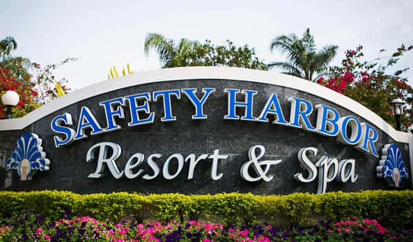 Front entrance sign for Safety Harbor Resort & Spa, surrounded by lush tropical landscaping and blooming flowers, welcoming guests to a tranquil Florida getaway.