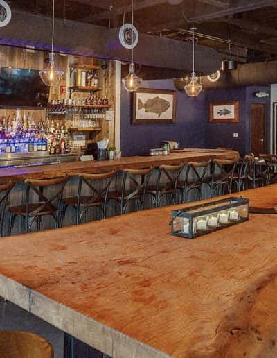 Rustic-chic bar interior at Water Oak Seafood and Steak Restaurant, featuring exposed ceilings, pendant lighting, a fully stocked bar, and wooden counter seating in Safety Harbor, Florida.