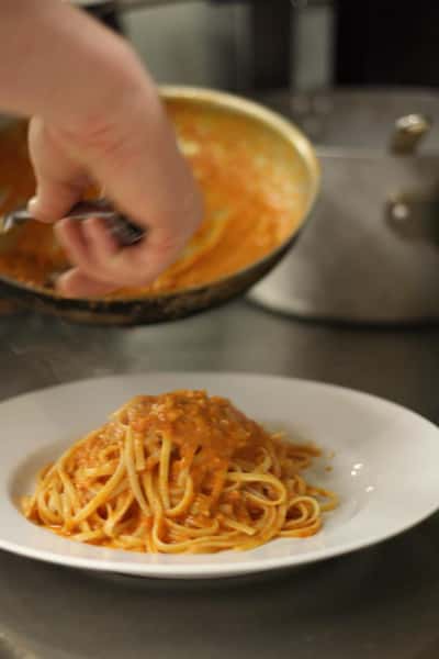 chef topping spaghetti with sauce in a plate