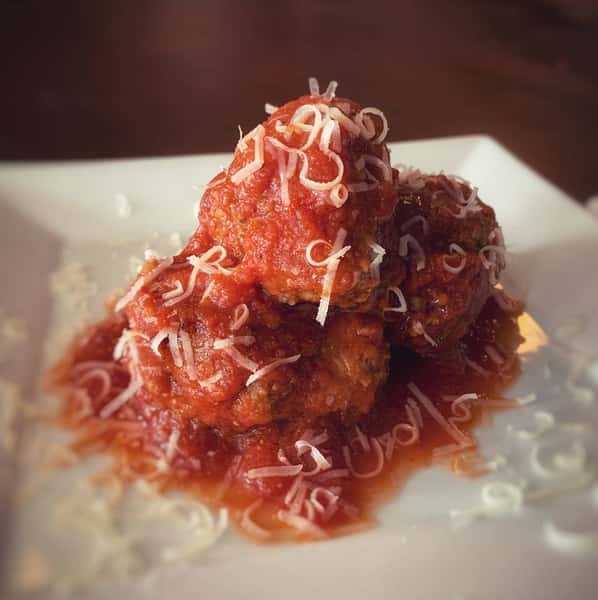 Meatballs stacked on each other with tomato sauce and grated cheese