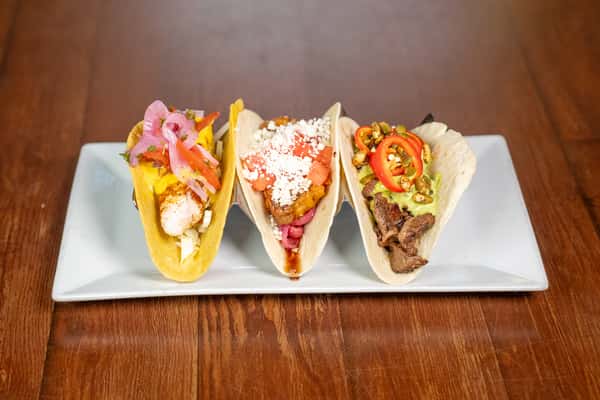 A fish taco, pork taco and steak taco on a plate
