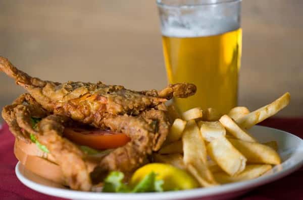 fried blue crab on a roll with a side of fries and a beer