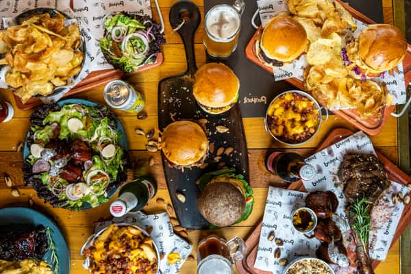 Vibrant overhead spread of gourmet burgers, loaded fries, fresh salads, and assorted craft beers at a casual burger restaurant — perfect for group dining.