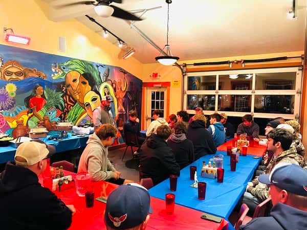 Dining room scene with guests seated at long tables in a brightly painted, mural filled space.