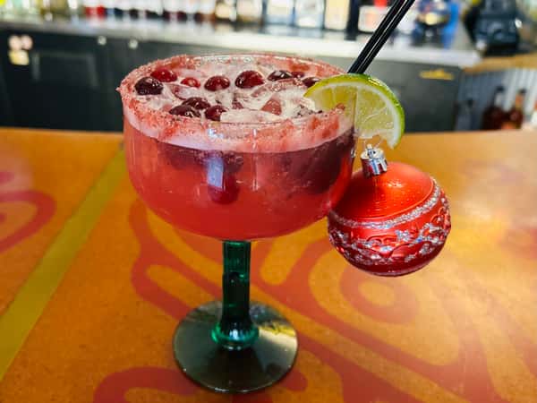 Red frozen margarita in a stemmed glass with a lime wedge and a small ornament beside it.