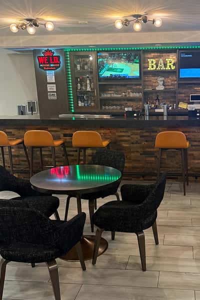 Modern hotel bar lounge with wood-paneled bar, high stools, cozy lounge seating, illuminated bar shelves, and TV screens creating a relaxed social atmosphere.