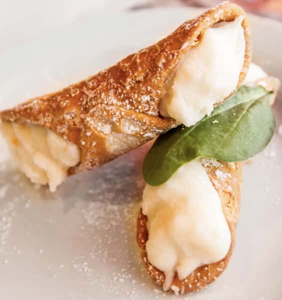 Close-up of classic Italian cannoli dessert filled with sweet ricotta cream, dusted with powdered sugar and garnished with a fresh mint leaf.