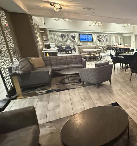 Modern hotel lounge seating area with leather sofas, round tables, contemporary lighting, and TV screens creating a comfortable social space inside a hotel lobby bar.