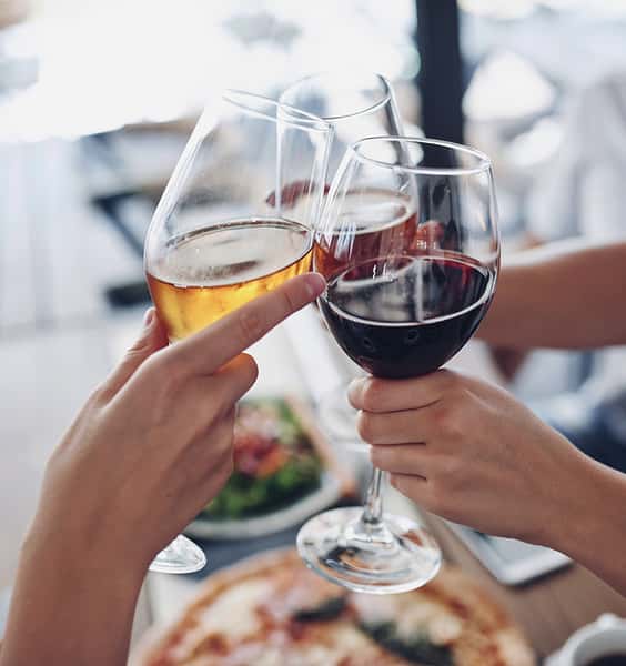 Guests clinking glasses of red and white wine over a restaurant table, capturing a celebratory dining moment with blurred food in the background.