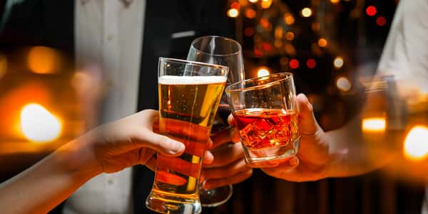 Guests clinking glasses of beer, red wine, and a whiskey cocktail in a warmly lit bar, capturing a celebratory nightlife moment with glowing candlelight ambiance.