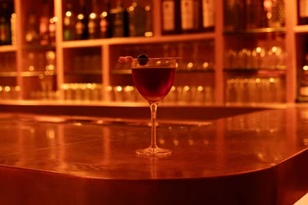 Refined cocktail garnished with a flower and dark berry, elegantly presented in a stemmed glass on a glossy bar counter—capturing the essence of a high-end cocktail lounge experience.