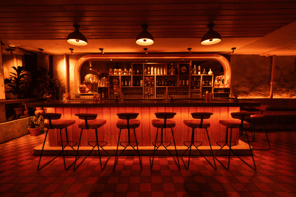 Stylish cocktail bar with plush velvet stools, a glowing wooden counter, and an illuminated back bar stocked with premium spirits, set in a moody, warmly lit lounge atmosphere.