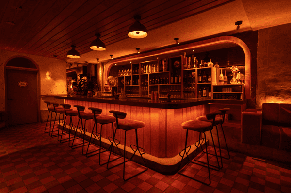 Elegant cocktail bar interior featuring a backlit wooden bar with velvet bar stools, an illuminated liquor display, and cozy red booth seating—ideal for nightlife, date nights, or modern lounge experiences.