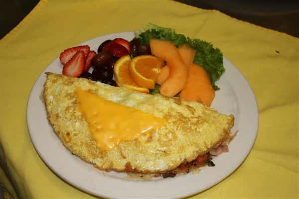 omlette filled with various meats and topped with cheese, with various side fruits