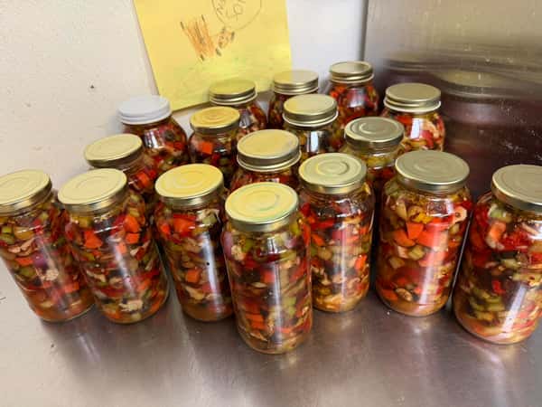assorted jars of pickled peppers and vegetables arranged on a prep table in a kitchen