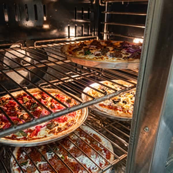 Four pizzas with various toppings baking inside an oven.