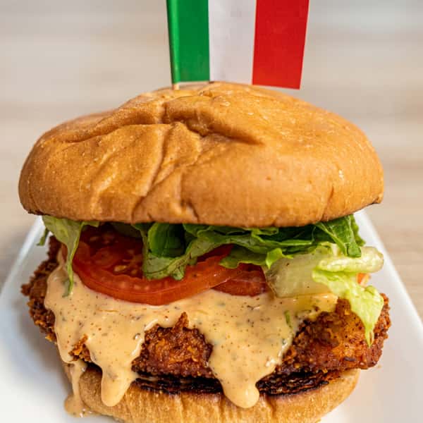 Crispy chicken sandwich with lettuce, tomatoes, creamy sauce, and an Italian flag toothpick.