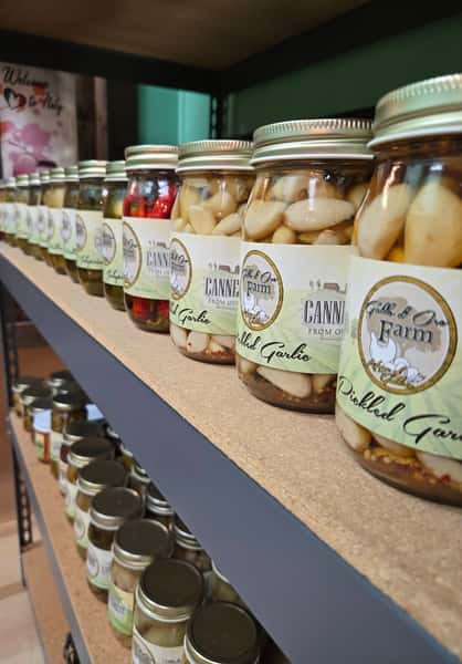 shelves of pickled vegetables in glass jars including garlic cloves and mixed produce in a market setting