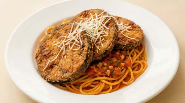 breaded eggplant parmesan slices over spaghetti with marinara sauce and grated cheese