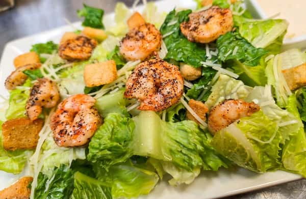 Shrimp Caesar salad with fried shrimp, croutons, parmesan cheese, and creamy dressing on a white platter.