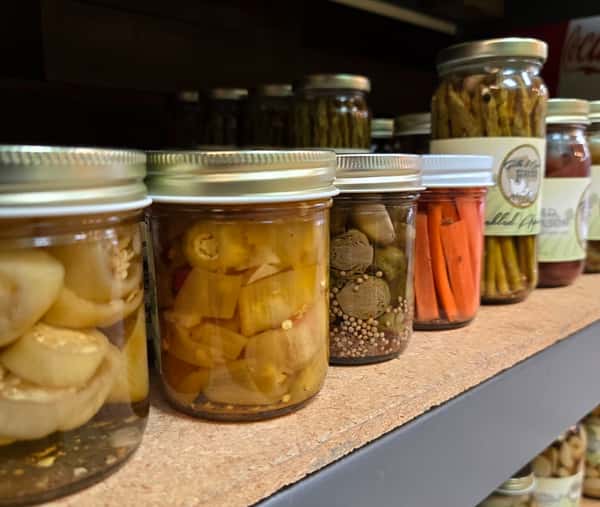 assorted pickled vegetables including carrots peppers and garlic in glass jars on store shelves