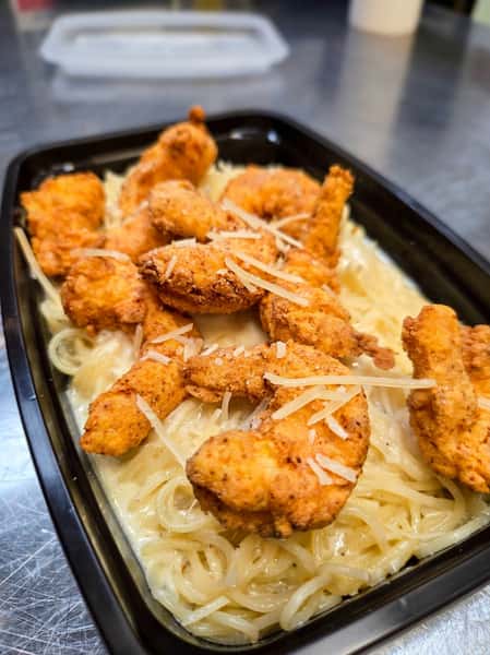 Fried chicken or shrimp over linguine pasta with a creamy white sauce and shredded cheese in a black tray.