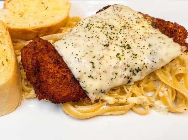 Chicken fettuccine alfredo with parmesan cheese, black pepper, and garlic bread on a white plate.