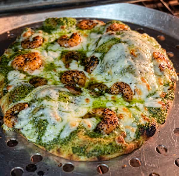 Pesto shrimp pizza with melted mozzarella cheese on a perforated metal pizza pan.