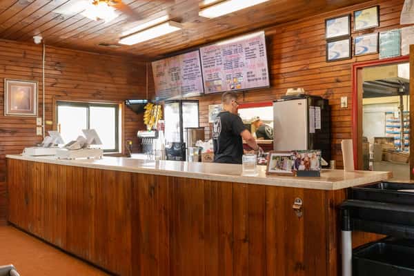 Restaurant interior showing a warm wooden service counter with coffee equipment and menu boards on the wall