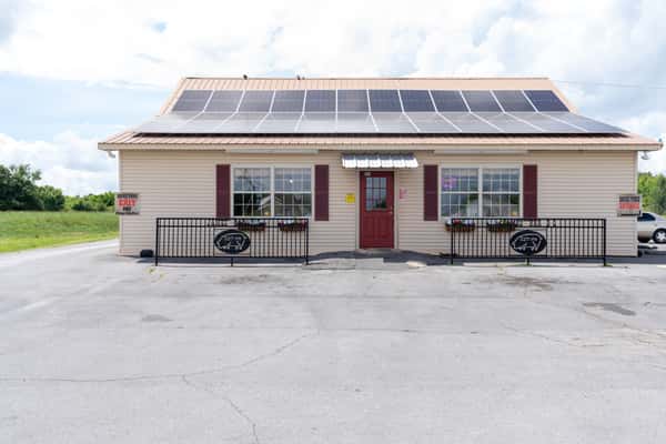 Exterior of the James BBQ restaurant building with solar panels on the roof, a red front door, and parking area