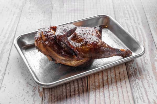 A golden-brown roasted half chicken served in a silver metal baking tray