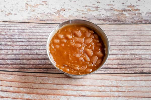 A bowl of slow-cooked BBQ baked beans served on a rustic wooden surface