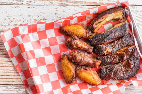 BBQ pork ribs and smoked chicken wings served on red and white checkered paper