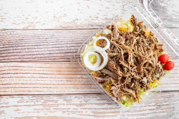 A BBQ salad with pulled smoked meat, fresh greens, and a creamy dressing served in a bowl on a rustic wooden surface
