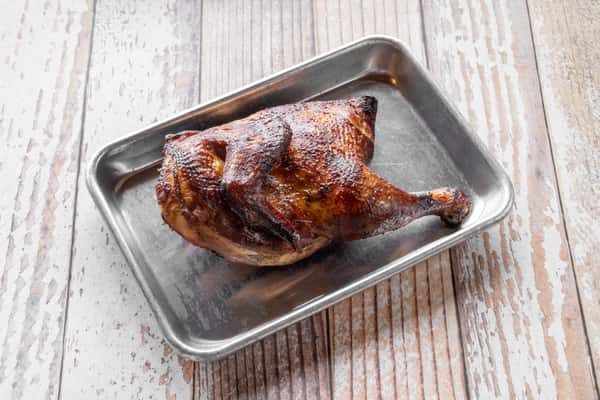 A golden-brown roasted half chicken served in a silver metal baking tray