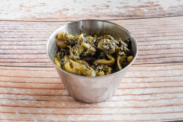 A metal cup filled with slow-cooked Southern turnip greens on a wooden surface
