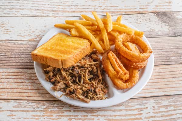 A BBQ plate with pulled smoked meat, golden french fries, onion rings, and cornbread on a white plate