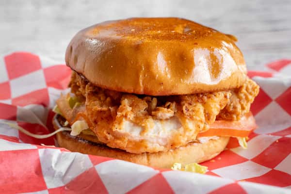 A crispy fried chicken sandwich on a toasted brioche bun, served on red and white checkered paper