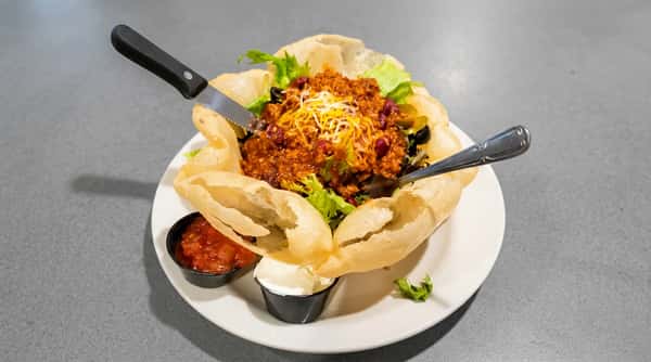 Chili with beans and shredded cheese in a crispy tortilla bowl, served with salsa and sour cream.