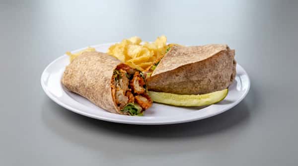 A cheesesteak sandwich cut in half, revealing steak and onions, served with potato chips and a pickle spear on a white plate.