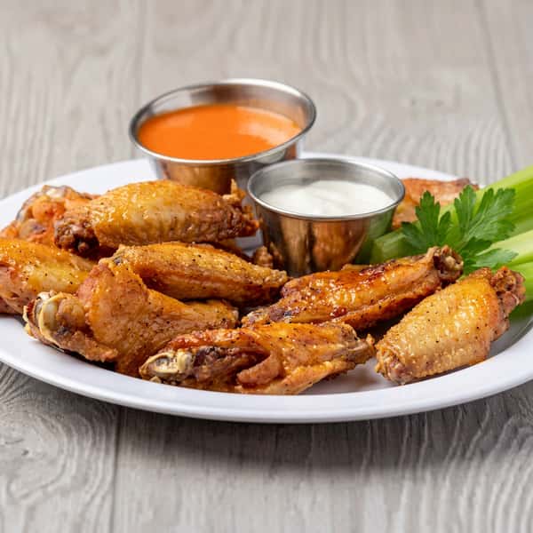 Plate of chicken wings with two dipping sauces and celery sticks.