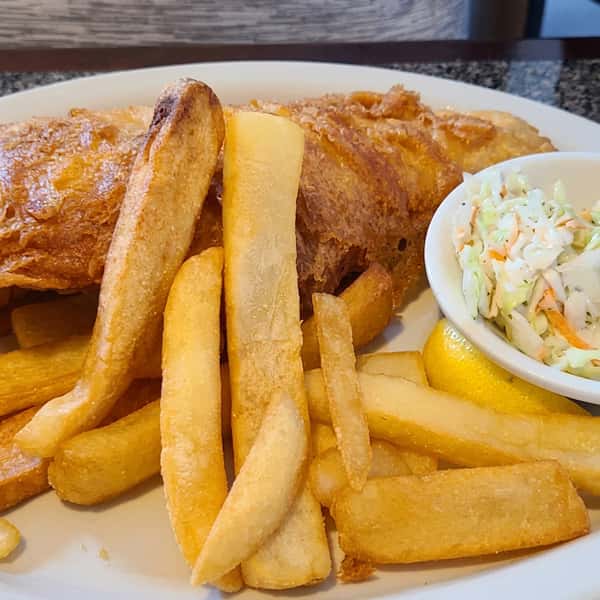Fish and chips with ketchup and two small cups of tartar sauce on a white plate.