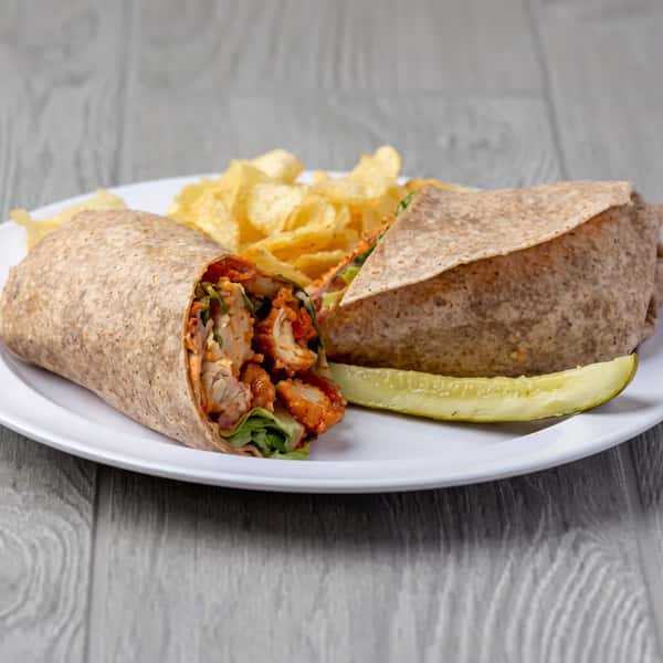 Chicken tender wrap with lettuce, tomatoes, and sauce on a white plate with potato chips and a pickle spear.