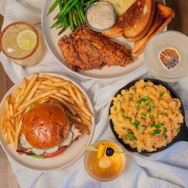 Comfort food spread featuring a fried chicken plate with toast and green beans, burger with fries, skillet mac and cheese, and cocktails.
