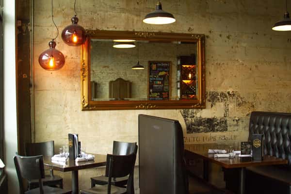 Cozy dining area with black leather booths, vintage mirror, exposed concrete walls, and warm pendant lighting.