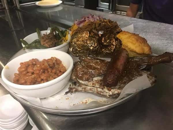 Meat platter served with baked potato, beans, collard greens and corn bread on the side