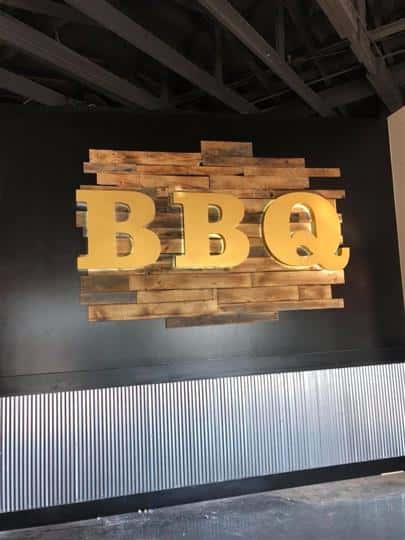 Mounted sign on the wall with the letters BBQ against a wooden background