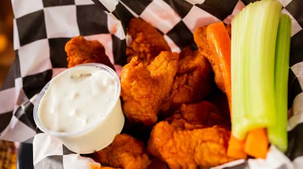 Buffalo chicken tenders in a checkerboard paper container with ranch dip, carrot, and celery sticks.
